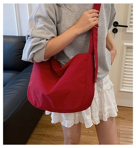 Detailed side view of the large red canvas crossbody bag worn in a casual daily outfit
