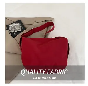 Detail view of the red nylon dumpling bag with adjustable strap on white bedding