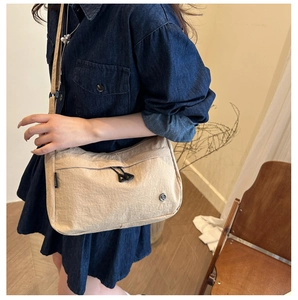 Detail view of a beige nylon crossbody bag featuring an adjustable strap and zipper pocket