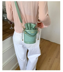 Detail of mint green bucket bag showing textured fabric, gold hardware, and drawstring
