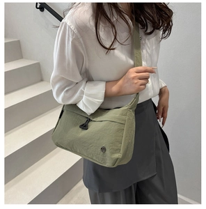 Detailed macro view of moss green nylon shoulder bag with circular metal logo and zip