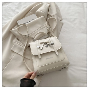 Close-up of cream handbag featuring bow decoration, heart pendant and fashion logo