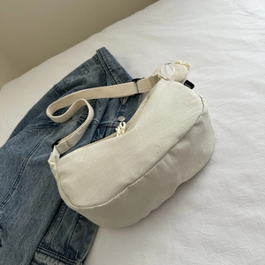 Detail view of beige crescent bag with adjustable strap and buckle on denim fabric