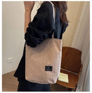 Detail of minimalist khaki nylon tote bag featuring a brand label and pleated texture