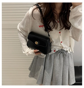 Close-up of black glossy leather bag featuring a round gold buckle and slim shoulder strap