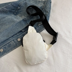 Close-up of beige nylon crossbody bag with black adjustable strap and buckle on denim