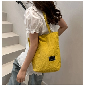 Detail of a bright yellow canvas tote bag with a black brand logo patch and shoulder straps