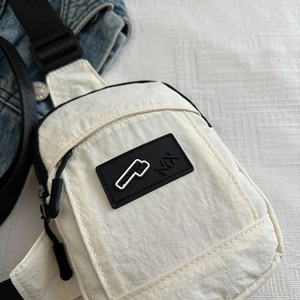 Detail of white nylon crossbody bag featuring a black rubber logo patch and adjustable strap