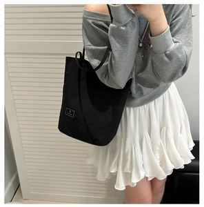 Detail of black nylon tote bag with square logo label worn on shoulder by a model