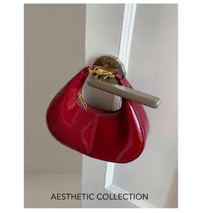 Detail of red patent leather hobo bag with moon shape and golden metal buckle clasp