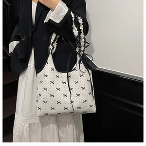 Detail of white bow print tote bag with ruffled handle and black ribbon on a model