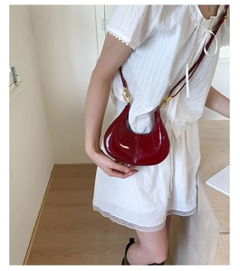 Close-up of wine red patent leather crescent bag with gold hardware on white dress