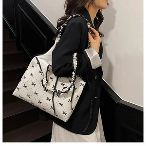 Detail of off-white tote bag with black bow print and ruffled frill shoulder strap