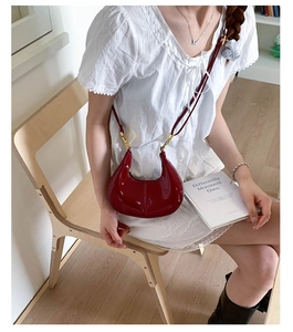 Detail view of deep red patent leather dumpling bag with elegant gold metal buckles