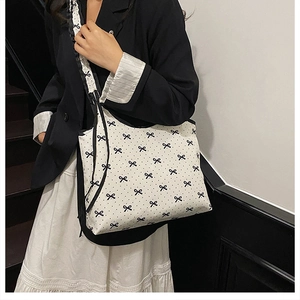 Close-up of a white canvas tote bag with black bow and polka dot patterns on a model