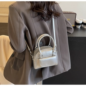 Silberne Mini-Bowlingtasche mit Knitteroptik, getragen von einem Modell im gemütlichen Café