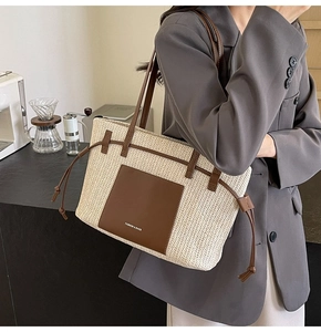 Detail of a large woven straw tote bag with brown leather accents on a model's shoulder