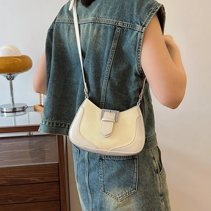 Minimalist cream crescent shoulder bag with silver buckle worn in a stylish home setting