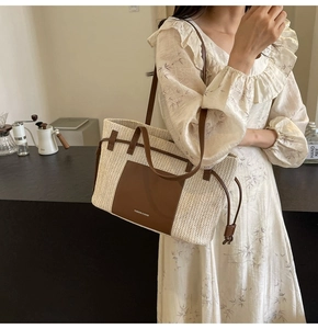 Detail of large beige woven straw tote bag featuring brown leather patch and straps