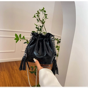 Detail of black glossy crocodile embossed bucket bag with silver chain and tassels