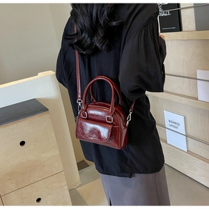 Nahaufnahme einer glänzenden tiefroten Mini-Muscheltasche mit Silberschnallen und Trageriemen