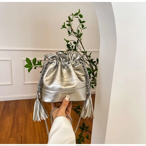 Detail of silver metallic bucket bag with fringe accents and chain strap on a drawstring closure