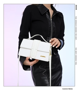 Detail of white embossed leather handbag with gold logo against black contrast outfit