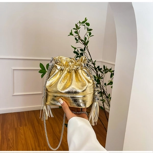 Close-up of gold crocodile embossed leather bucket bag with silver chain and fringe details