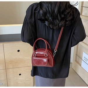 Detailansicht einer burgunderroten Mini-Umhängetasche aus Lackleder am Modell