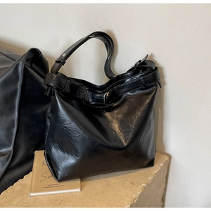 Detail of glossy pleated leather texture and silver buckle on large black tote bag