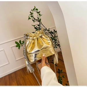 Detail of gold bucket bag with crocodile pattern and metallic fringe accents