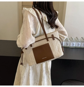 Detail of woven straw tote bag featuring a brown leather pocket and dual shoulder straps