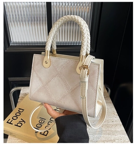 Detail of cream crossbody bag featuring woven handle, cross-pattern texture, and gold hardware