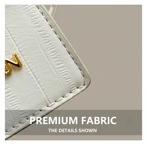 Detail of white embossed leather handbag featuring golden metal letter and fine stitching