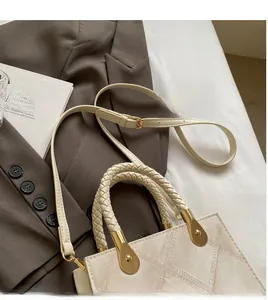 Detail of the woven handle and adjustable long shoulder strap on a beige square handbag