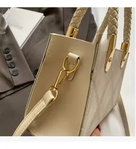 Detail of beige tote bag with gold hardware hooks and woven cylindrical top handle