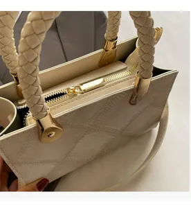 Close-up of smooth golden metal zipper and woven handle detail on beige crossbody bag