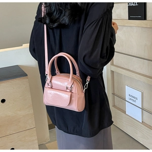 Detail der glänzenden rosa Mini-Boston-Tasche mit Rundgriffen an einem Model