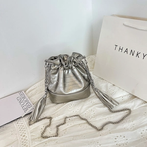 Silver glossy bucket bag with metal chain strap and tassels on white lace background