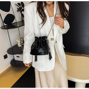 Dettaglio di una borsa a secchiello nera con coulisse, catene d'argento e frange sulla modella