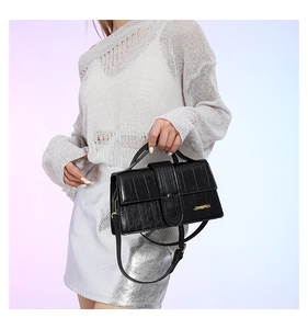 Close-up of black faux crocodile skin texture and gold logo on stylish square handbag