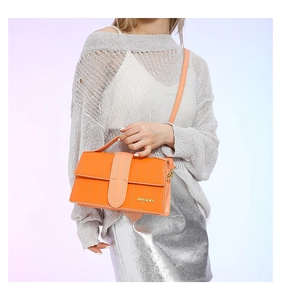 Detail of bright orange textured crossbody bag with gold logo and matching shoulder strap