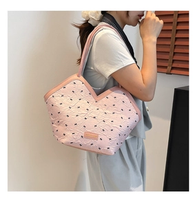 Close-up of pink pleated tote bag featuring black bow patterns and leather logo patch