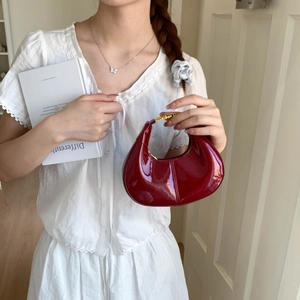 Detail of red patent leather crescent handbag with elegant gold metal handle and texture