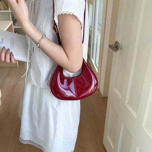 Detail of a dark red patent leather crescent bag with a high-gloss finish and gold buckle