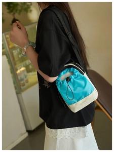 Vista lateral de bolso bandolera azul y beige con correa ajustable llevado por una modelo