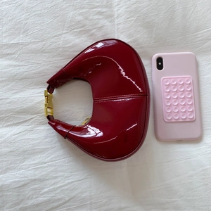 Top view of a glossy burgundy crescent handbag with a phone for size comparison