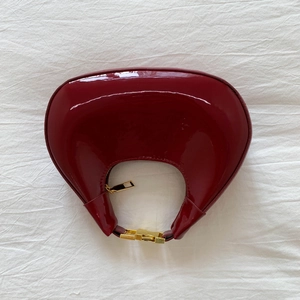 Detailed view of deep red patent leather crescent hobo bag with gold hardware