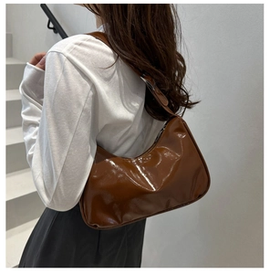 Detail of a dark brown patent leather crescent shoulder bag worn on a model's arm