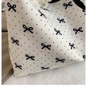 Close-up of canvas tote bag featuring black polka dots and delicate bow patterns